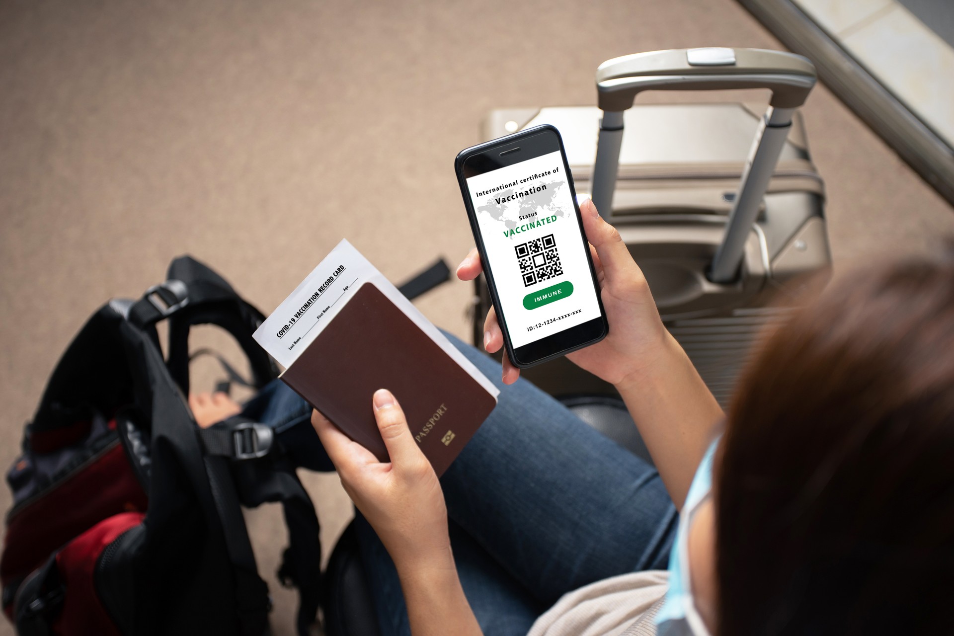 Smartphone on hand of woman traveler with health passport of vaccination certification in the airport. Certificate of vaccinated coronavirus. Travel concept during Covid-19 pandemic.